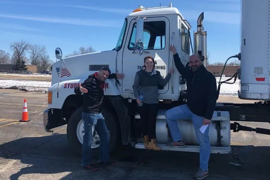 Truck driving students celebrate by a student driver semi after studying the Michigan CDL manual